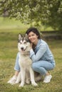 Beautiful brunette girl sitting on the grass with her funny friend malamute dog