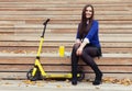 Beautiful brunette girl sitting on wooden steps with a glass and donuts. Yellow scooter stands next