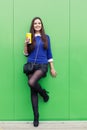 Beautiful brunette girl standing with a glass in his hand near the green wall and smiling at the camera Royalty Free Stock Photo