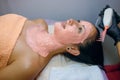 Beautiful brunette girl takes procedures in a spa salon, a master beautician applies a pink mask to her face and does massage with