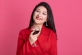 Beautiful brunette girl wearing red dress in studio against rosy background,adorable female with toothy smile standing with glass Royalty Free Stock Photo