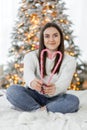 A beautiful brunette girl in a white sweater holding candy canes in the shape of heart against Christmas tree lights Royalty Free Stock Photo