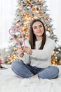 A beautiful brunette girl in a white sweater holding candy canes in the shape of heart against Christmas tree lights Royalty Free Stock Photo