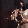 Beautiful and mysterious brunette in a gold dress and with a snake