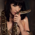 Beautiful and mysterious brunette in a gold dress and with a snake