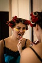 Beautiful brunette in home pajamas and curlers brushes her teeth near the mirror Royalty Free Stock Photo