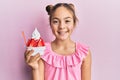 Beautiful brunette little girl eating strawberry ice cream looking positive and happy standing and smiling with a confident smile