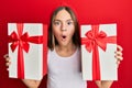 Beautiful brunette little girl holding gifts afraid and shocked with surprise and amazed expression, fear and excited face Royalty Free Stock Photo