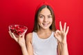 Beautiful brunette little girl holding red pepper doing ok sign with fingers, smiling friendly gesturing excellent symbol Royalty Free Stock Photo