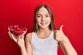 Beautiful brunette little girl holding red pepper smiling happy and positive, thumb up doing excellent and approval sign Royalty Free Stock Photo