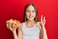 Beautiful brunette little girl holding salty biscuits in a bowl doing ok sign with fingers, smiling friendly gesturing excellent Royalty Free Stock Photo