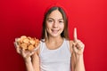 Beautiful brunette little girl holding salty biscuits in a bowl smiling with an idea or question pointing finger with happy face, Royalty Free Stock Photo