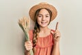 Beautiful brunette little girl holding spike wheat smiling with an idea or question pointing finger with happy face, number one Royalty Free Stock Photo