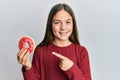 Beautiful brunette little girl holding tasty colorful doughnut smiling happy pointing with hand and finger Royalty Free Stock Photo