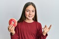 Beautiful brunette little girl holding tasty colorful doughnut smiling happy pointing with hand and finger to the side Royalty Free Stock Photo