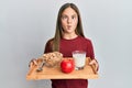 Beautiful brunette little girl holding tray with breakfast food making fish face with mouth and squinting eyes, crazy and comical