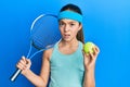 Beautiful brunette little girl playing tennis holding racket and ball clueless and confused expression Royalty Free Stock Photo