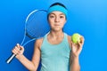 Beautiful brunette little girl playing tennis holding racket and ball puffing cheeks with funny face Royalty Free Stock Photo