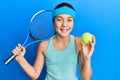 Beautiful brunette little girl playing tennis holding racket and ball smiling and laughing hard out loud because funny crazy joke Royalty Free Stock Photo