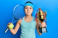 Beautiful brunette little girl playing tennis holding trophy puffing cheeks with funny face Royalty Free Stock Photo