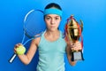 Beautiful brunette little girl playing tennis holding trophy skeptic and nervous, frowning upset because of problem Royalty Free Stock Photo