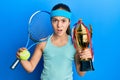 Beautiful brunette little girl playing tennis holding trophy skeptic and nervous, frowning upset because of problem Royalty Free Stock Photo