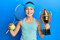 Beautiful brunette little girl playing tennis holding trophy smiling with a happy and cool smile on face Royalty Free Stock Photo