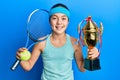 Beautiful brunette little girl playing tennis holding trophy smiling and laughing hard out loud because funny crazy joke Royalty Free Stock Photo