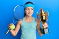 Beautiful brunette little girl playing tennis holding trophy smiling looking to the side and staring away thinking Royalty Free Stock Photo