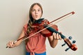 Beautiful brunette little girl playing violin making fish face with mouth and squinting eyes, crazy and comical