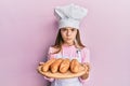 Beautiful brunette little girl wearing baker uniform holding homemade bread skeptic and nervous, frowning upset because of problem Royalty Free Stock Photo
