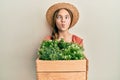 Beautiful brunette little girl wearing gardener hat holding wooden plant pot making fish face with mouth and squinting eyes, crazy