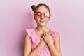 Beautiful brunette little girl wearing heart shaped sunglasses smiling with hands on chest, eyes closed with grateful gesture on Royalty Free Stock Photo