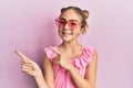 Beautiful brunette little girl wearing heart shaped sunglasses smiling and looking at the camera pointing with two hands and Royalty Free Stock Photo