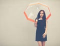 Beautiful brunette with long hair in a short black dress standing under a transparent umbrella. Colorful hipster photo