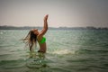 Beautiful brunette with long hair stands waist-deep in the ocean and splashes her hands in water. Young slender girl in bright Royalty Free Stock Photo