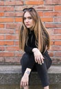 beautiful brunette with long hair, student, sits against the background of a brick wall Royalty Free Stock Photo