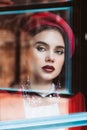 Beautiful brunette model with blue eyes in a red beret is looking through the glass at the camera. Skin retouching Royalty Free Stock Photo