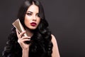 Beautiful brunette model: curls, classic makeup and red lips with a bottle of hair products. The beauty face. Royalty Free Stock Photo