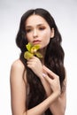 A beautiful brunette nude shoulders girl sensually holds a flower of an orchid in her hands. Nude make-up. Healthy smooth skin Royalty Free Stock Photo