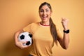 Beautiful brunette player woman playing soccer using football ball over yellow background screaming proud and celebrating victory Royalty Free Stock Photo