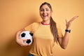 Beautiful brunette player woman playing soccer using football ball over yellow background very happy and excited, winner Royalty Free Stock Photo