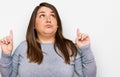 Beautiful brunette plus size woman wearing casual clothes pointing up looking sad and upset, indicating direction with fingers,