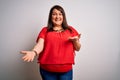 Beautiful brunette plus size woman wearing casual red t-shirt over isolated white background smiling cheerful with open arms as Royalty Free Stock Photo