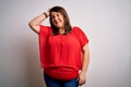 Beautiful brunette plus size woman wearing casual red t-shirt over isolated white background smiling confident touching hair with Royalty Free Stock Photo