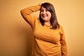 Beautiful brunette plus size woman wearing casual sweater over isolated yellow background smiling confident touching hair with Royalty Free Stock Photo