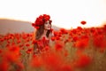 Beautiful brunette in red poppies field. Happy smiling teen girl portrait with wreath on head enjoying in poppy flowers nature bac Royalty Free Stock Photo