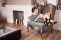 Beautiful brunette rich saucy woman in elegant dress sitting on a chair in a room with classic interior drinking wine