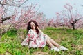 beautiful brunette sitting in a green clearing by a flowering tree Royalty Free Stock Photo