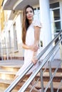 Beautiful brunette stands on the steps, a shopping center, pink dress Royalty Free Stock Photo